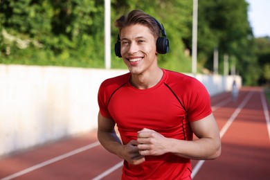 Photo of Sporty man with headphones running at stadium, space for text