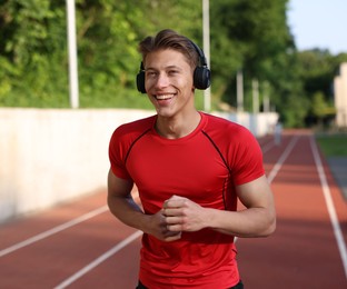 Photo of Sporty man with headphones running at stadium