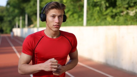 Photo of Sporty man with headphones running at stadium, space for text