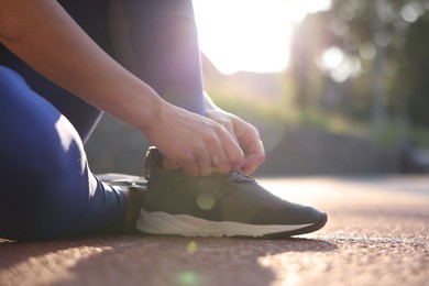Photo of Woman tying shoelace of sneaker at stadium, closeup. Space for text