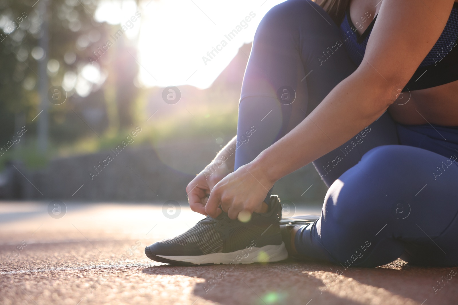 Woman tying shoelace of sneaker at stadium, closeup. Space for text Photo of Woman tying shoelace of sneaker at stadium, closeup. Space for text