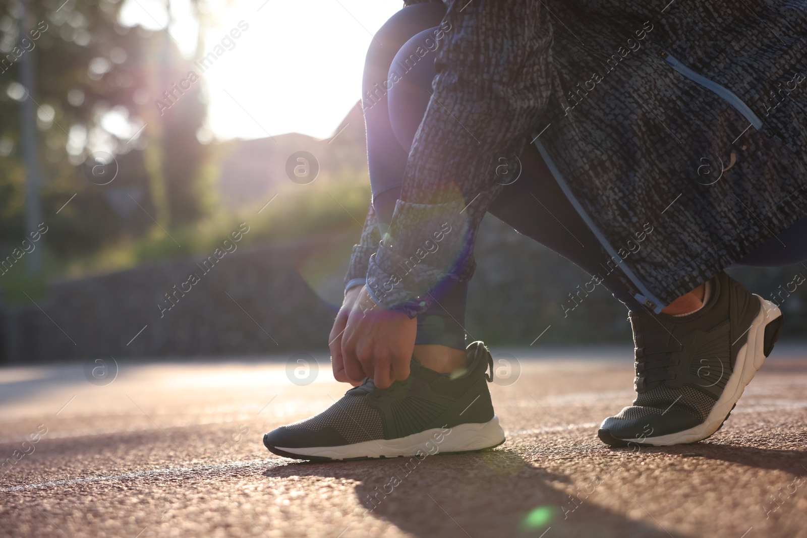 Woman tying shoelace of sneaker at stadium, closeup. Space for text Photo of Woman tying shoelace of sneaker at stadium, closeup. Space for text