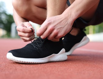 Photo of Man tying shoelace of black sneaker at stadium, closeup