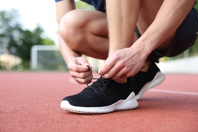 Photo of Man tying shoelace of black sneaker at stadium, closeup. Space for text
