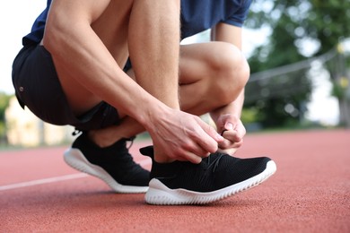Photo of Man tying shoelace of black sneaker at stadium, closeup