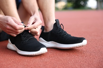 Photo of Man tying shoelace of black sneaker at stadium, closeup