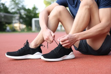 Photo of Man tying shoelace of black sneaker at stadium, closeup