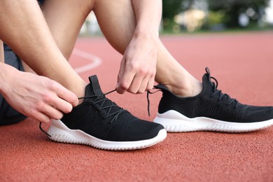 Photo of Man tying shoelace of black sneaker at stadium, closeup