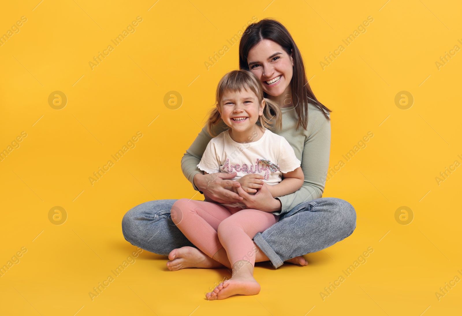 Happy mother and her cute daughter on orange background Photo of Happy mother and her cute daughter on orange background