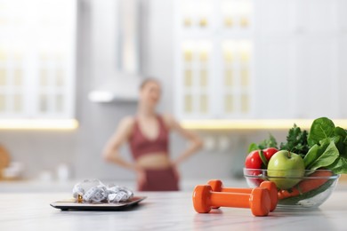 Photo of Slim woman in sportswear posing indoors, focus on kitchen scale, healthy food, dumbbells and measuring tape