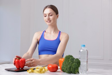 Photo of Woman weighting bell pepper on kitchen scale at white marble table indoors