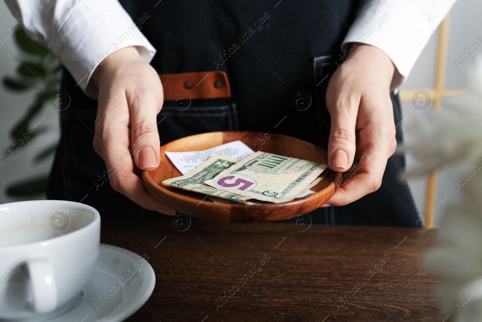 Photo of Waitress holding tips and receipt at wooden table in cafe, closeup