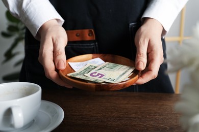 Photo of Waitress holding tips and receipt at wooden table in cafe, closeup