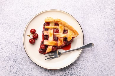 Photo of Piece of tasty cherry pie, berries and fork on grey textured table, top view