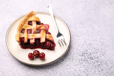 Photo of Piece of tasty cherry pie, berries and fork on grey textured table. Space for text