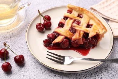 Photo of Piece of tasty cherry pie, berries and fork on grey textured table, closeup