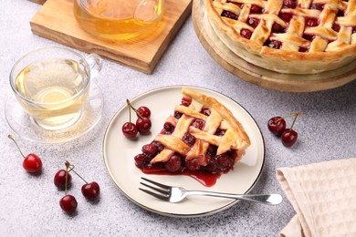 Photo of Piece of tasty cherry pie, berries and tea on grey textured table