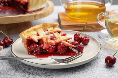 Photo of Piece of tasty cherry pie, berries and fork on grey textured table, closeup