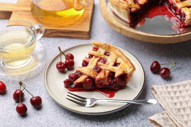 Photo of Piece of tasty cherry pie, berries and fork on grey textured table, closeup
