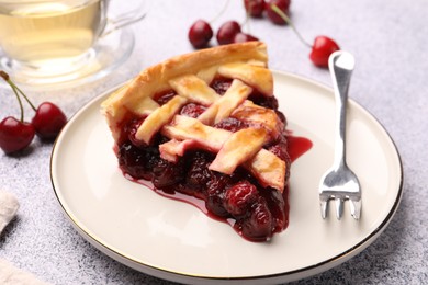 Photo of Piece of tasty cherry pie, berries and fork on grey textured table, closeup