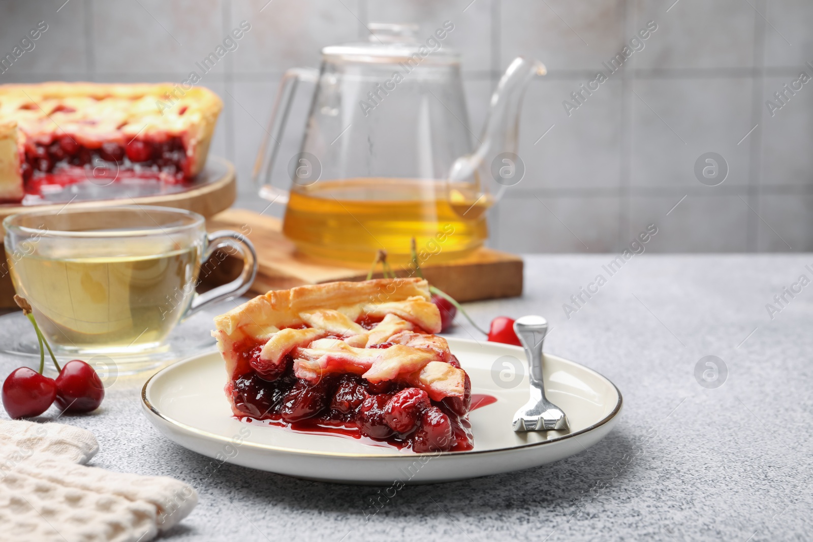 Photo of Piece of tasty cherry pie, berries and tea on grey textured table against tiled wall, closeup