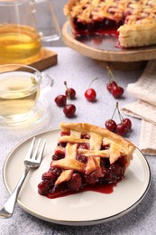 Photo of Piece of tasty cherry pie, berries and tea on grey textured table, closeup