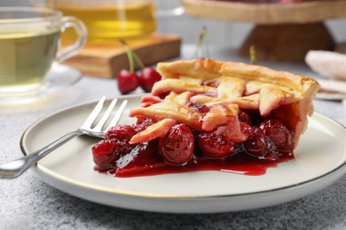 Photo of Piece of tasty cherry pie and fork on grey textured table, closeup