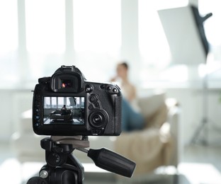 Photo of Woman on sofa in studio, focus on video camera recording her