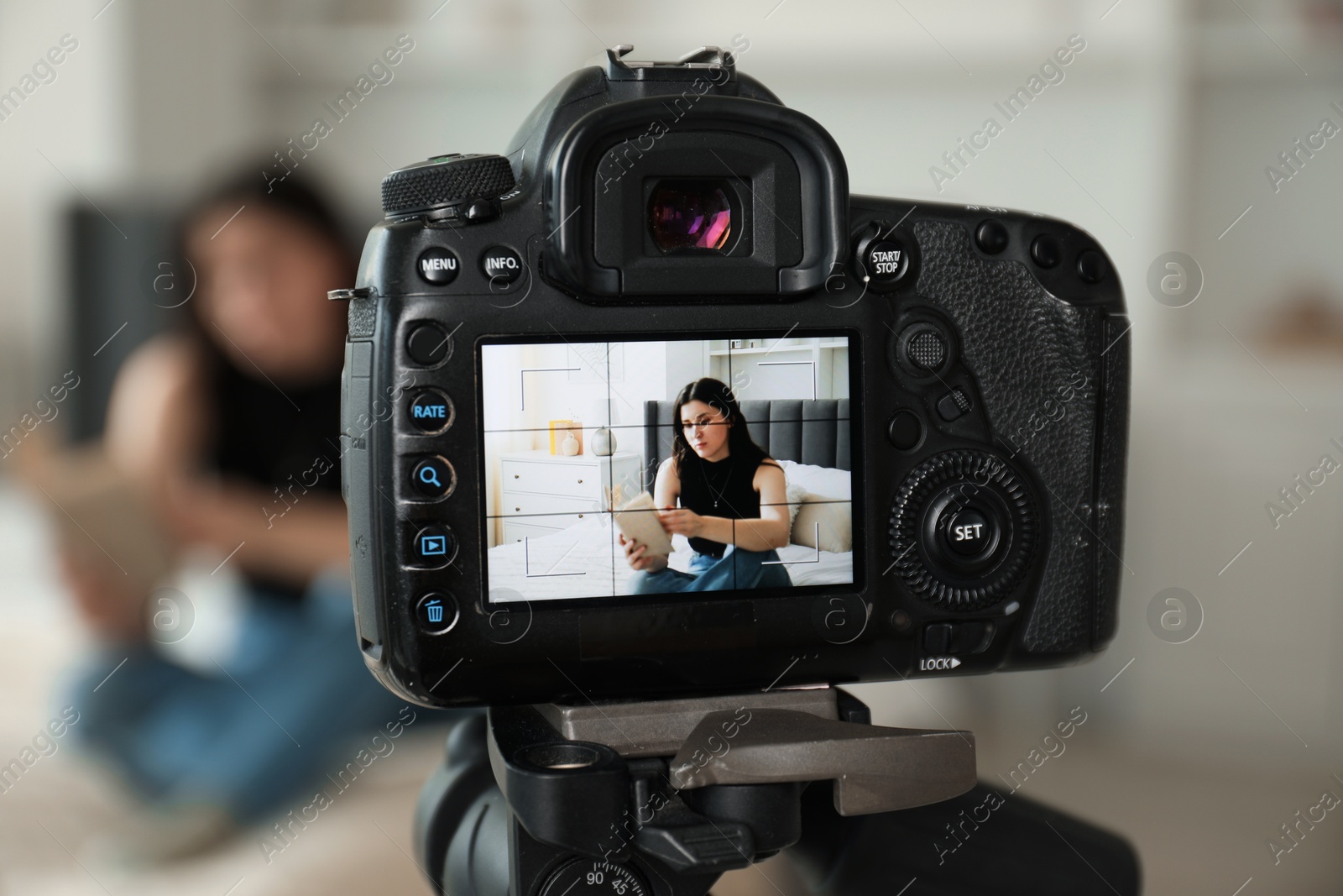 Woman reading book on bed in studio, focus on video camera recording her Photo of Woman reading book on bed in studio, focus on video camera recording her