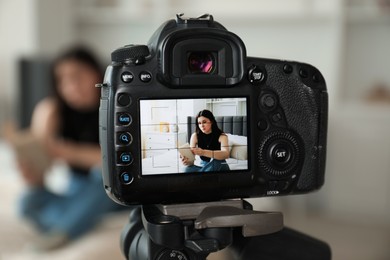 Photo of Woman reading book on bed in studio, focus on video camera recording her