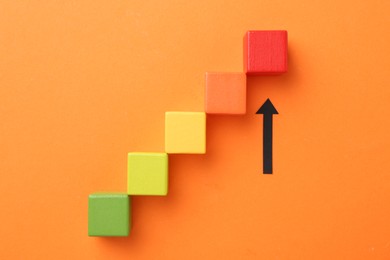 Photo of Maximum. Arrow pointing at colorful cubes on orange background, top view