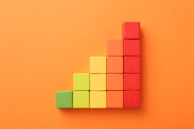 Photo of Maximum. Colorful cubes on orange background, top view