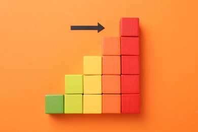 Photo of Maximum. Arrow pointing at colorful cubes on orange background, top view