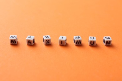Photo of Word Maximum made of cubes on orange background