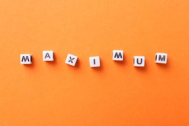 Photo of Word Maximum made of cubes on orange background, top view