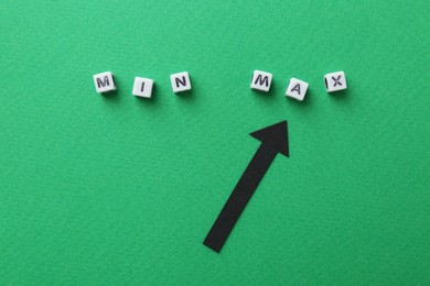 Photo of Words Min and Max made of cubes with arrow pointing at it on green background, flat lay