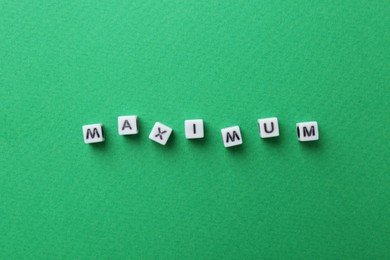 Photo of Word Maximum made of cubes on green background, top view