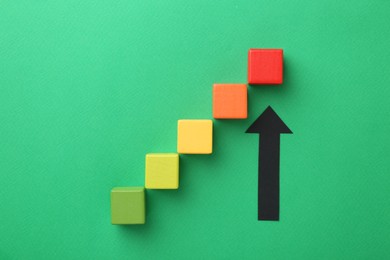 Photo of Maximum. Arrow pointing at colorful cubes on green background, flat lay