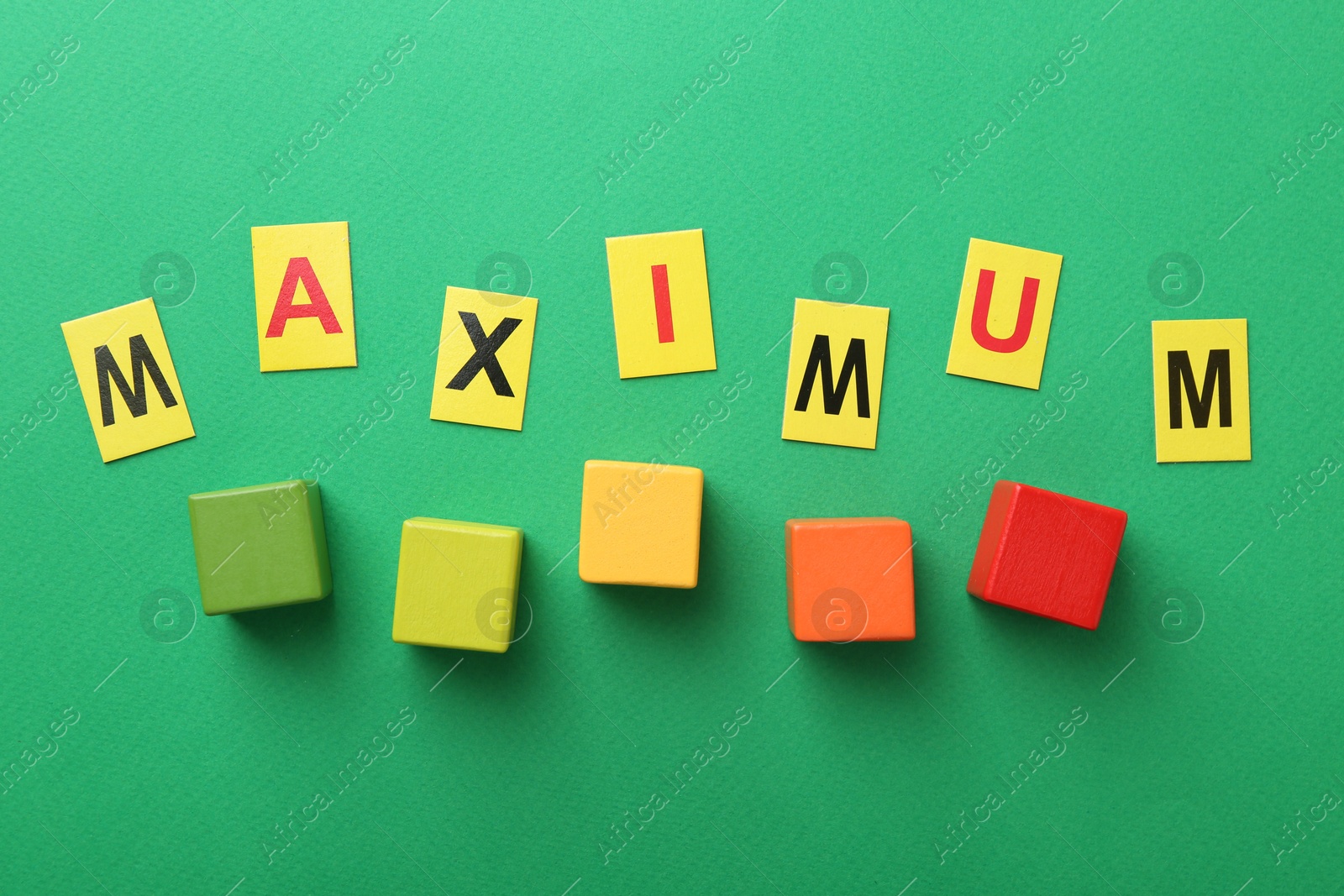 Word Maximum and colorful cubes on green background, flat lay Photo of Word Maximum and colorful cubes on green background, flat lay