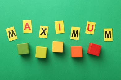 Photo of Word Maximum and colorful cubes on green background, flat lay