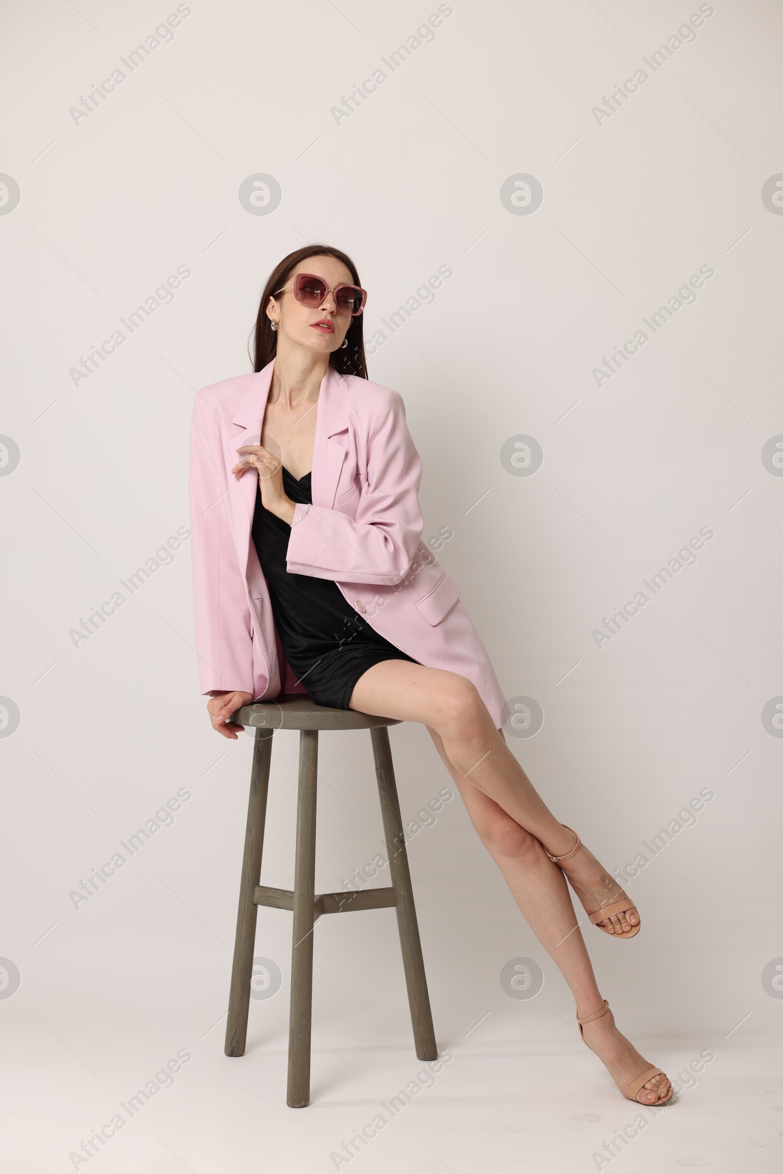 Beautiful woman in stylish outfit sitting on chair against white background Photo of Beautiful woman in stylish outfit sitting on chair against white background