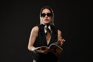 Photo of Beautiful woman in stylish outfit with fashion magazine on black background
