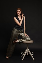Photo of Beautiful woman in stylish outfit sitting on chair against black background