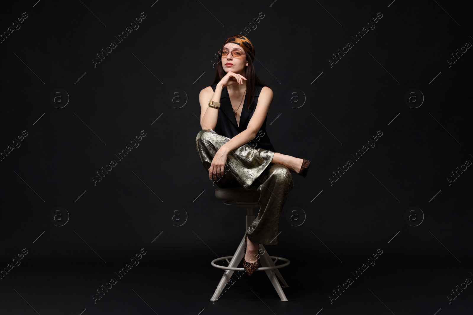 Beautiful woman in stylish outfit sitting on chair against black background Photo of Beautiful woman in stylish outfit sitting on chair against black background