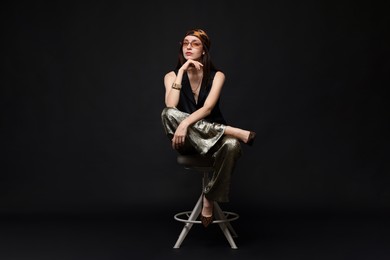 Photo of Beautiful woman in stylish outfit sitting on chair against black background