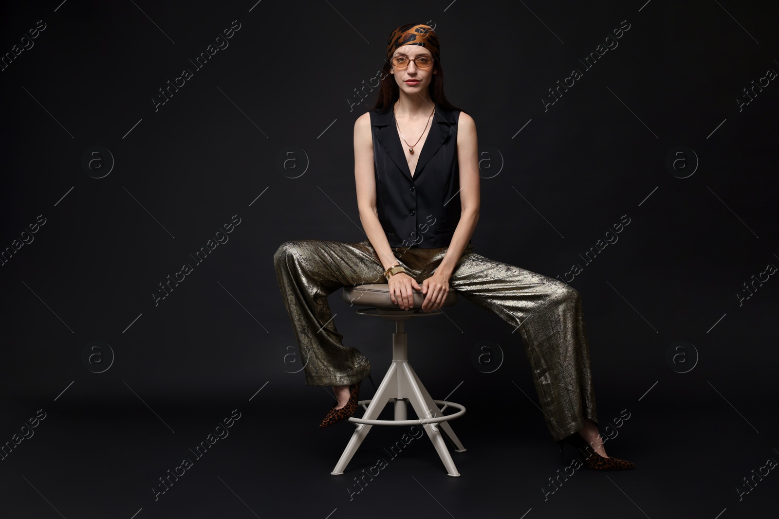 Beautiful woman in stylish outfit sitting on chair against black background Photo of Beautiful woman in stylish outfit sitting on chair against black background