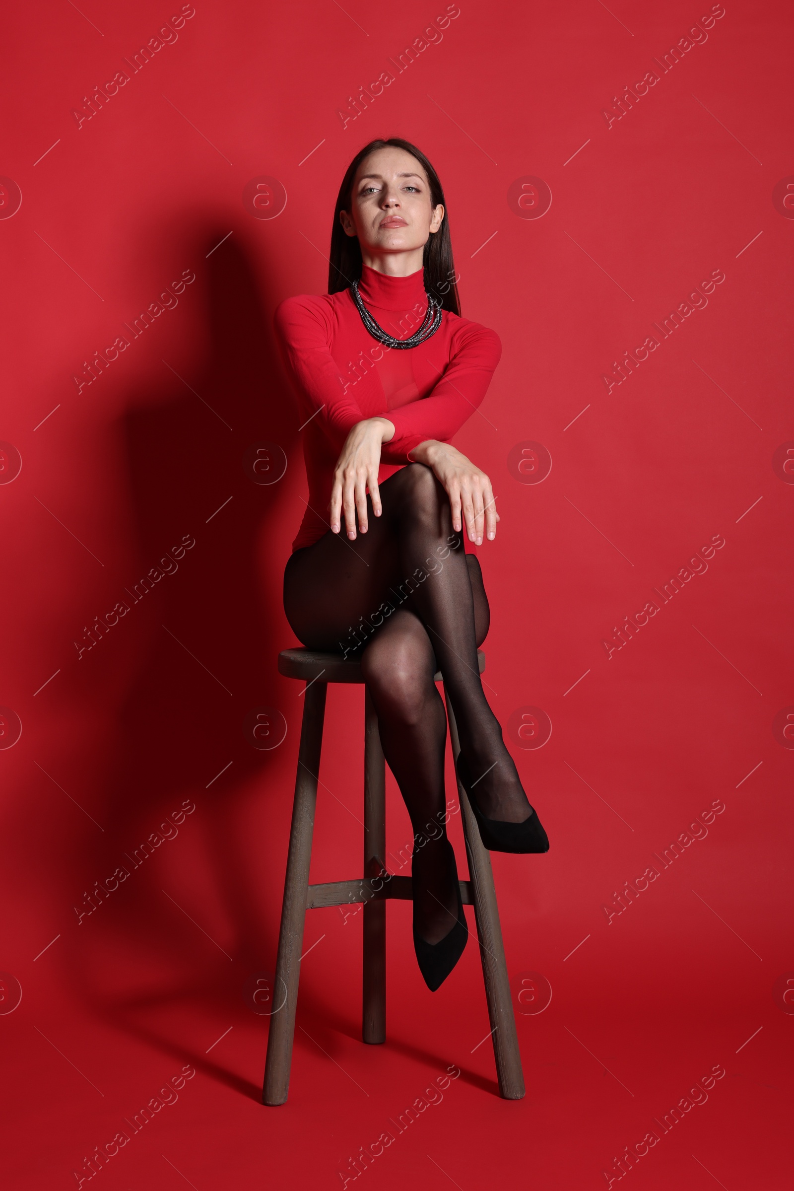 Beautiful woman in stylish outfit and chair on red background Photo of Beautiful woman in stylish outfit and chair on red background