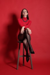 Photo of Beautiful woman in stylish outfit and chair on red background