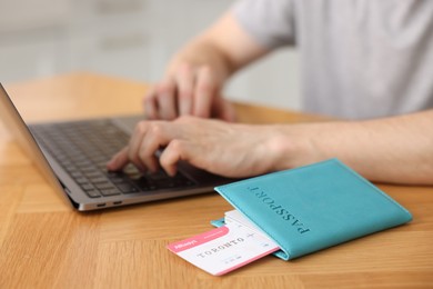 Photo of Man using laptop at wooden table with passport and flight ticket indoors, closeup
