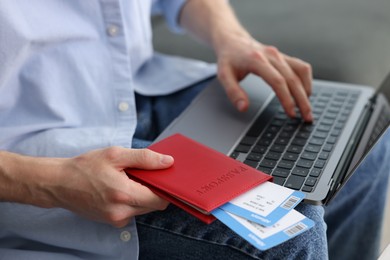 Photo of Man with passport and flight tickets using laptop indoors, closeup